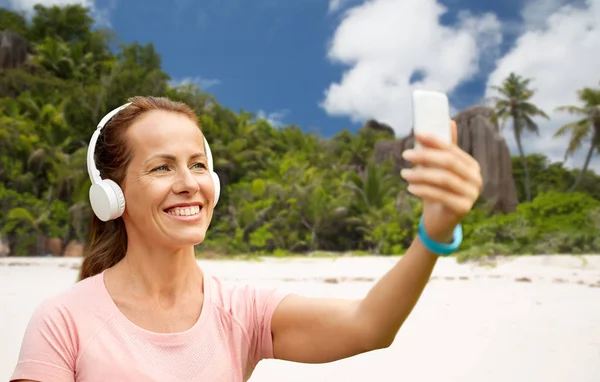 Woman in phones takes selfie by cellphone on beach — Stock Photo, Image