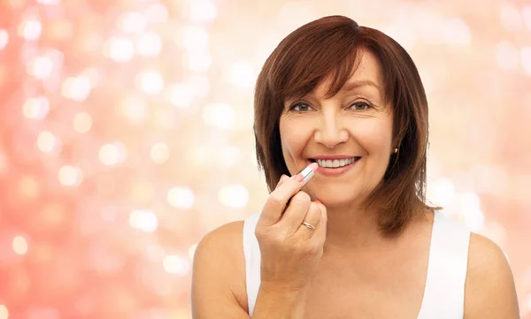 Sorridente donna anziana che applica il rossetto alle labbra — Foto Stock