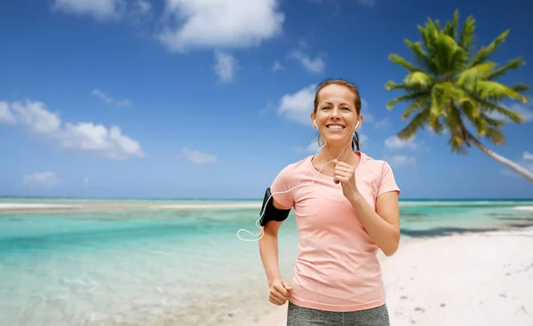 Frau mit Kopfhörer und Armbinde läuft am Strand — Stockfoto