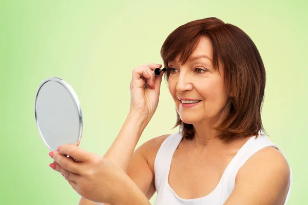 Donna anziana sorridente con specchio che applica mascara — Foto Stock