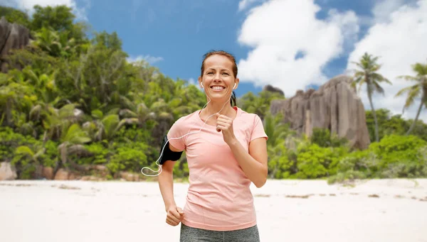 Mujer con auriculares y brazalete corriendo en la playa —  Fotos de Stock