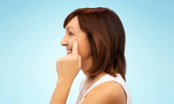 Perfil de la mujer mayor que señala las arrugas oculares — Foto de Stock