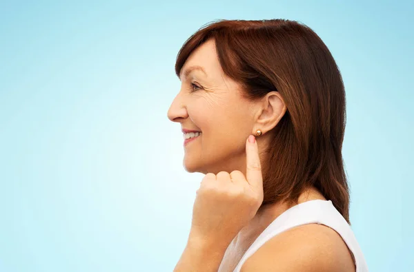 Sonriente mujer mayor señalando a su pendiente — Foto de Stock