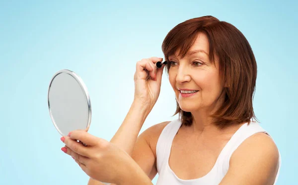 Femme âgée souriante avec miroir appliquant mascara — Photo