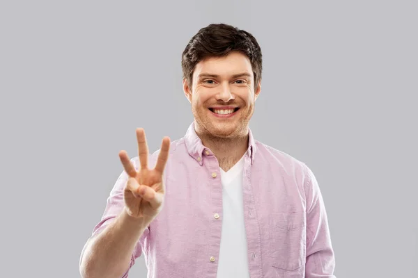 Junger Mann zeigt drei Finger über Grau — Stockfoto