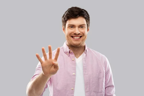 Νεαρός άνδρας δείχνει τέσσερα δάχτυλα πέρα από το γκρι — Φωτογραφία Αρχείου