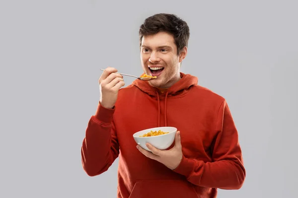 Usměvavý mladý muž v červených kapucí jíst obiloviny — Stock fotografie