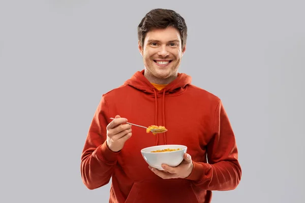 Leende ung man i röd huvtröja äta spannmål — Stockfoto