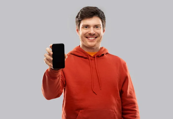 Sonriente hombre en sudadera con capucha roja mostrando teléfono inteligente negro — Foto de Stock