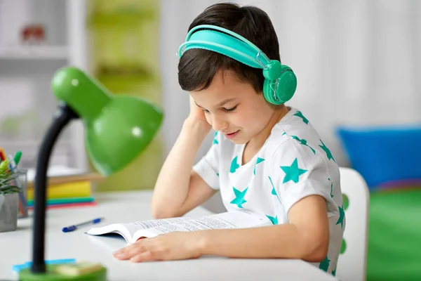 Jongen in hoofdtelefoon met leerboek thuis leren — Stockfoto