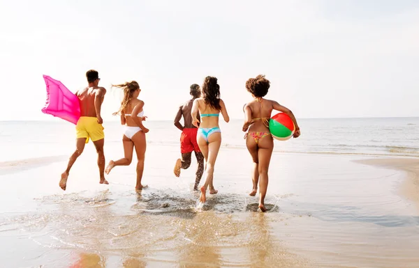 Friends run with beach ball and swimming mattress — Stock Photo, Image
