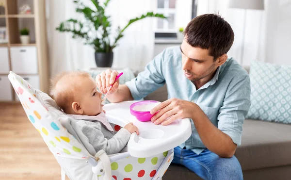 Padre alimentación feliz bebé en silla alta en casa —  Fotos de Stock