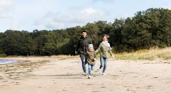 Família feliz correndo ao longo da praia de outono — Fotografia de Stock