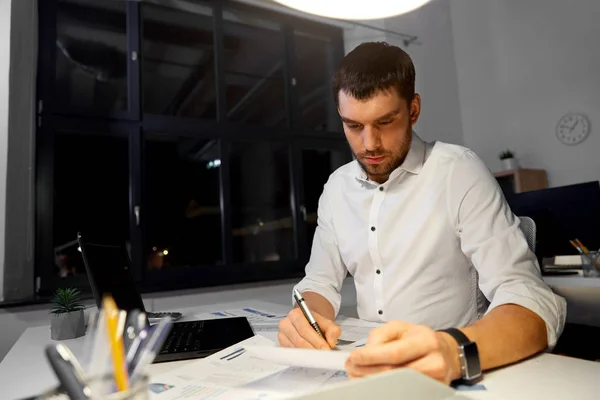 Homme d'affaires avec papiers et ordinateur portable au bureau de nuit — Photo