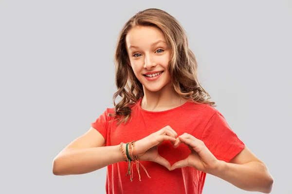 Souriant adolescent fille en rouge faisant coeur de la main — Photo