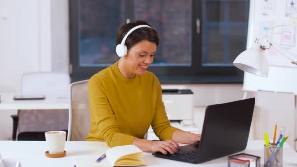 Femme créative dans les écouteurs avec ordinateur portable au bureau — Video