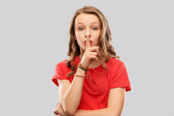 Дівчина-підліток у червоній футболці з пальцем на губах — стокове фото