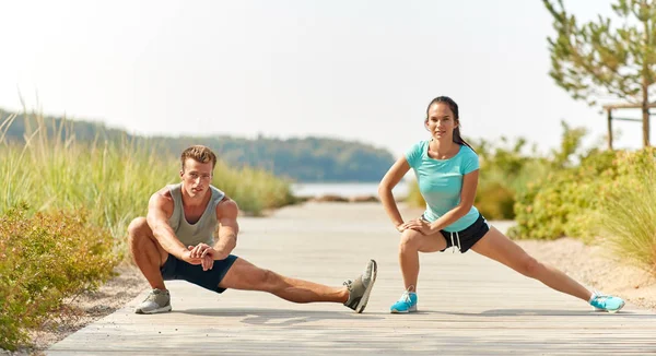 Glimlachend paar stretching benen op strand — Stockfoto