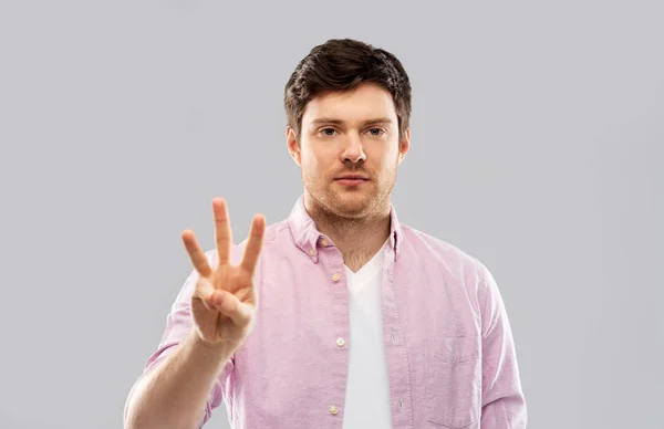 Mladý muž ukazuje tři prsty nad šedá — Stock fotografie