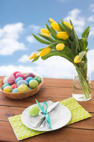 Easter eggs in basket, plates, cutlery and flowers — Stock Photo, Image