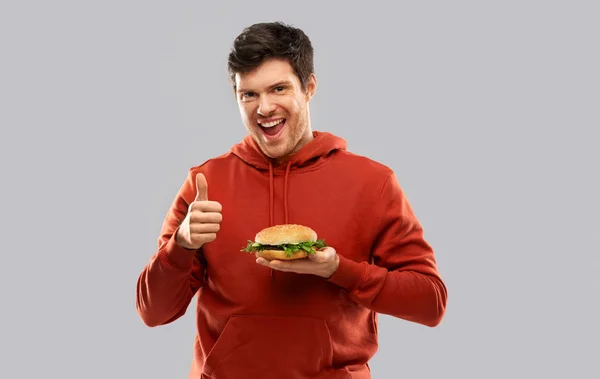 Feliz joven con hamburguesa mostrando los pulgares hacia arriba —  Fotos de Stock