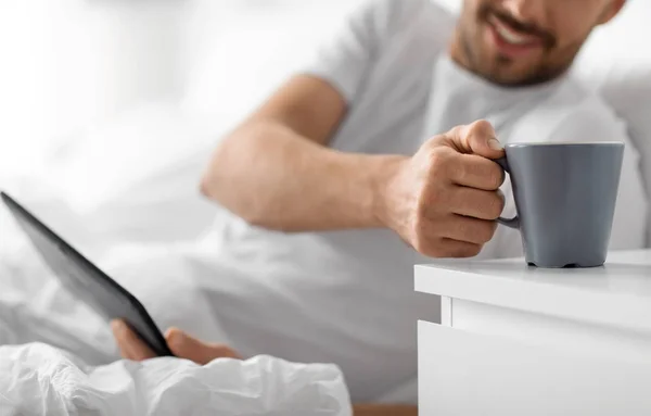 Férfi tabletta számítógép kávét iszik az ágyban Stock Kép