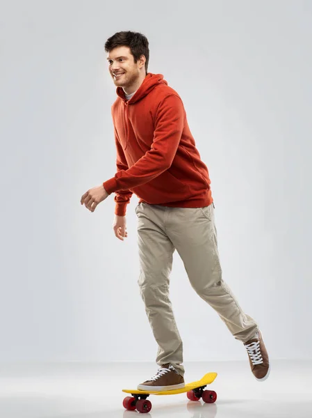 Smiling young man in hoodie riding on skateboard — Stock Photo, Image