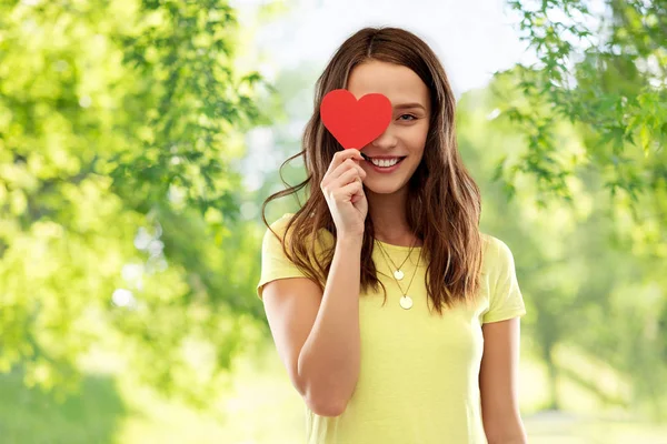 Улыбающаяся девочка-подросток, закрывающая глаза красным сердцем — стоковое фото