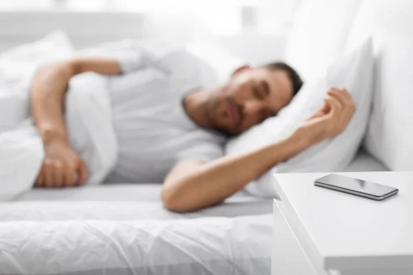 Smartphone na mesa de cabeceira perto de dormir homem — Fotografia de Stock