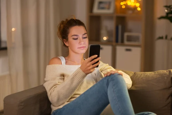 Mladá žena s smartphone doma večer — Stock fotografie