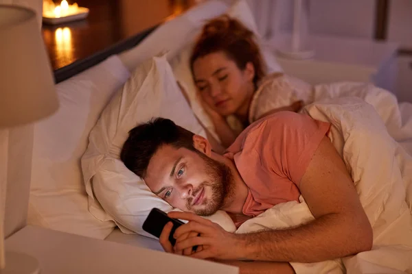 Hombre usando el teléfono inteligente mientras su novia está durmiendo — Foto de Stock