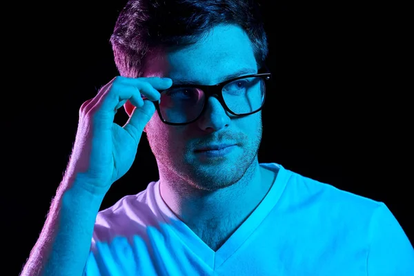 Man in glasses over neon lights in dark room — Stock Photo, Image