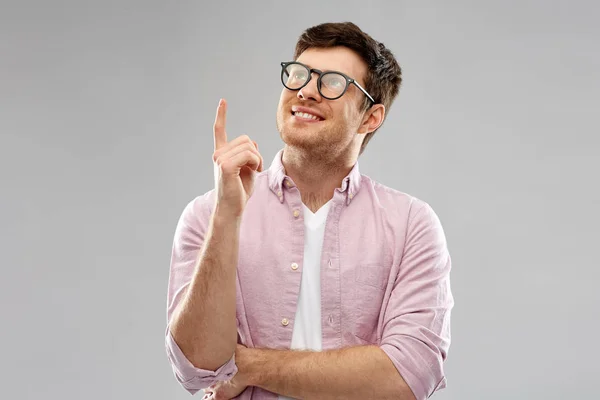 Sorridente giovane uomo in occhiali puntando il dito verso l'alto — Foto Stock