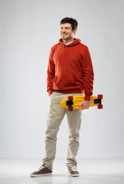 Jeune homme souriant en sweat à capuche avec skateboard court — Photo