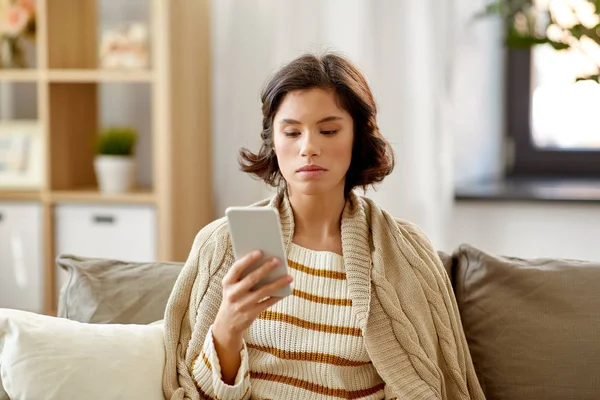 Λυπημένη γυναίκα στην κουβέρτα χρησιμοποιώντας το smartphone στο σπίτι — Φωτογραφία Αρχείου