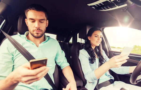 Hombre y mujer con teléfonos inteligentes que conducen en coche —  Fotos de Stock