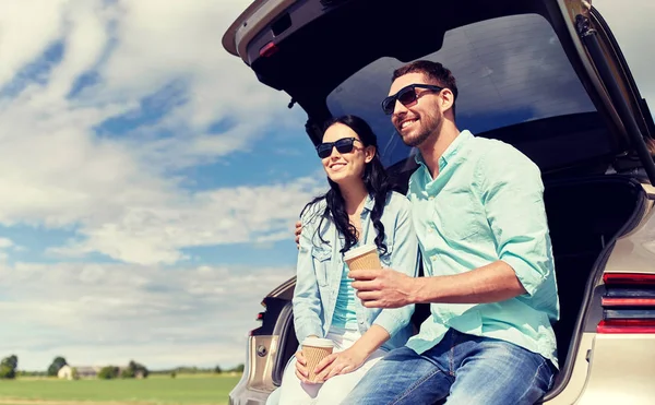 Happy couple with coffee at hatchback car trunk — Stock Photo, Image