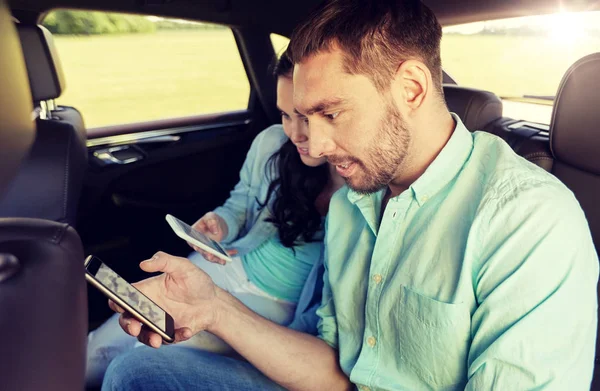 Casal com smartphones montando no banco de trás do carro — Fotografia de Stock