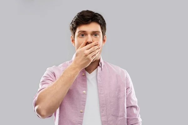 Shocked young man covering his mouth by hand — Stock Photo, Image