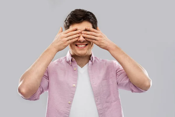 Homem fechando os olhos por mãos sobre fundo cinza — Fotografia de Stock