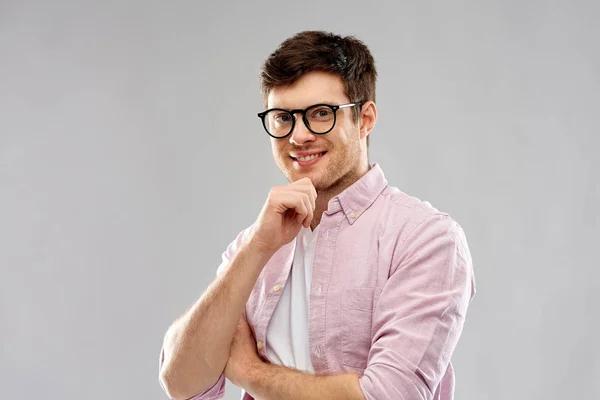 Uśmiechający się młody człowiek w okularach na szarym tle — Zdjęcie stockowe