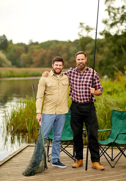 Friends with fishing rods and net at lake or river — Stock Photo, Image