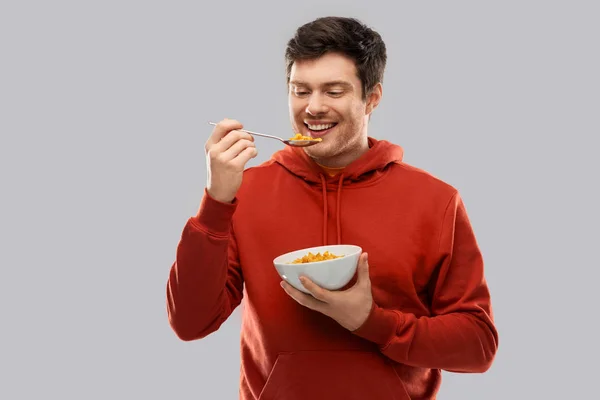 Mosolygó fiatal ember a piros kapucnis pulcsit, étkezési gabona — Stock Fotó