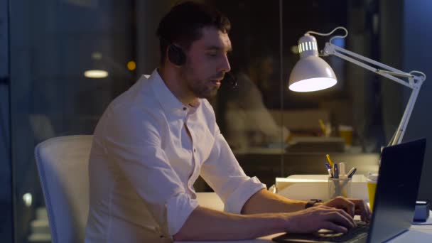 Hombre de negocios en auriculares con ordenador portátil en la oficina de noche — Vídeo de stock