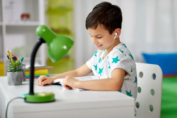 Student jongen in oortelefoons lezen boek thuis — Stockfoto