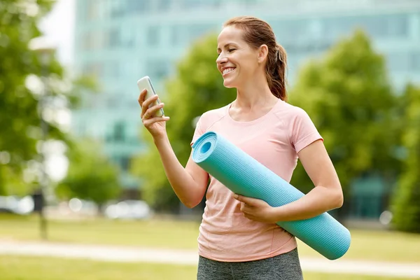 Mulher com tapete de exercício e smartphone no parque — Fotografia de Stock