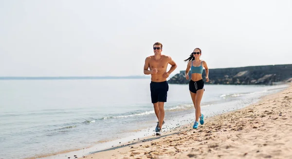 Пара в спортивной одежде бегает по пляжу — стоковое фото