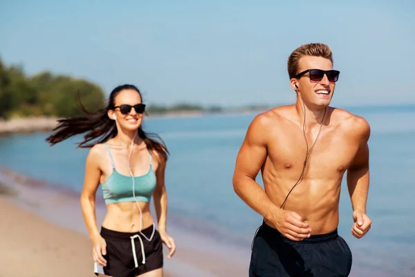 Par med hörlurar som löper längs stranden — Stockfoto