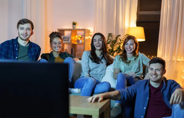 Amici felici guardando la tv a casa la sera — Foto Stock