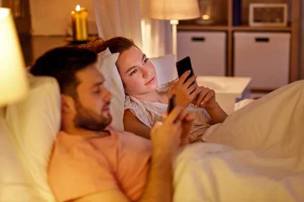 Пара с помощью смартфонов в постели ночью — стоковое фото